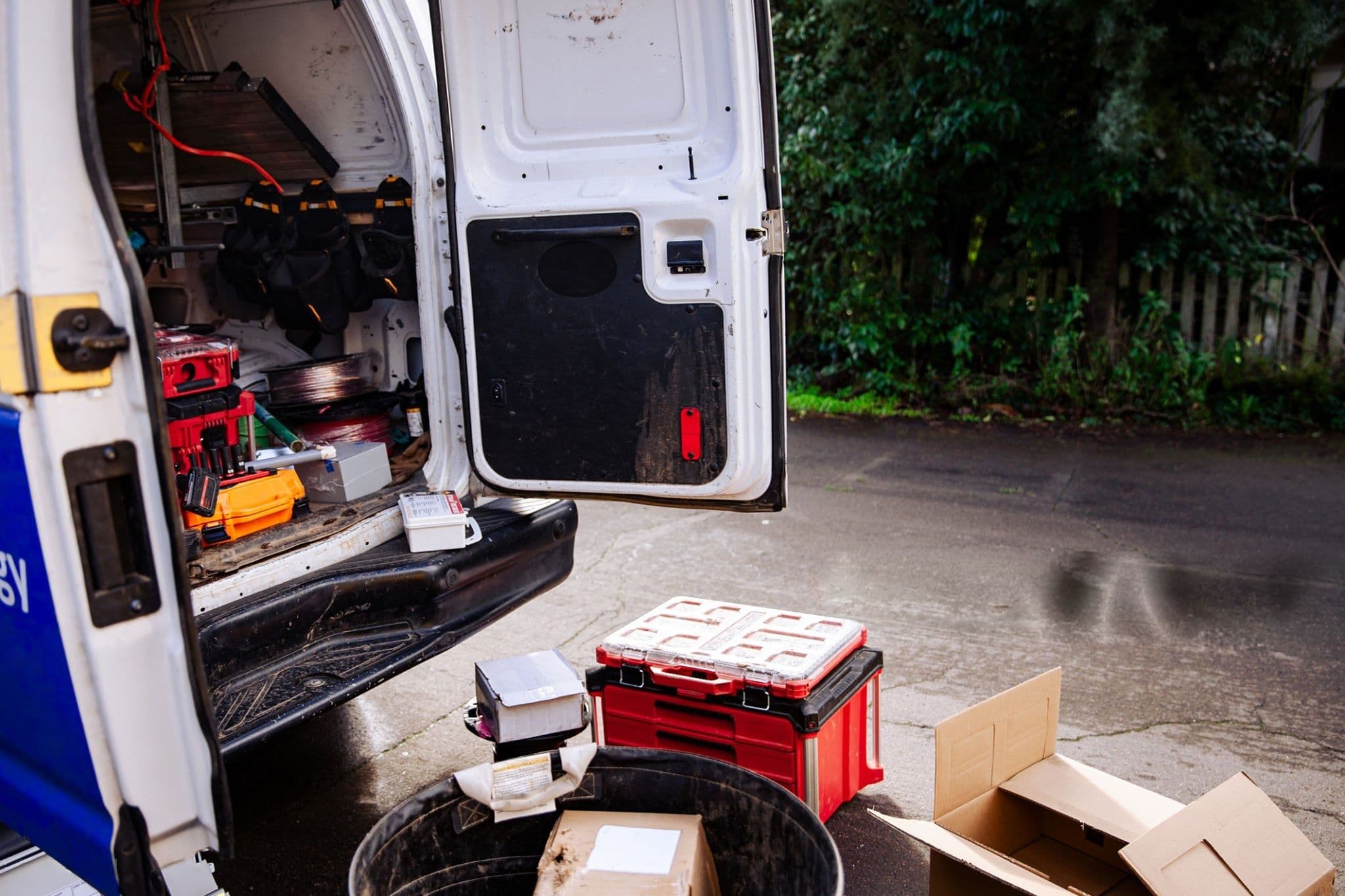 The open rear doors of a working electrician’s van on a driveway, tools and cable drums inside
