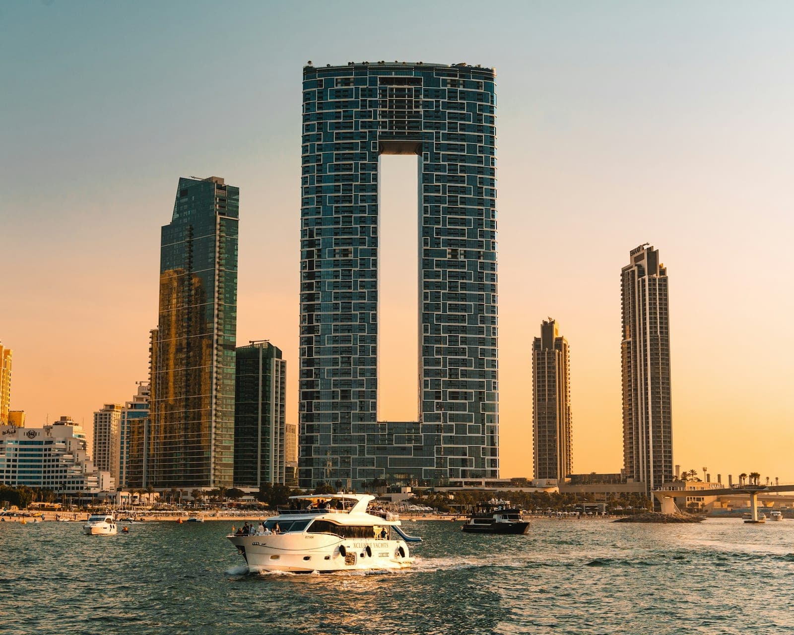 Modern skyscrapers and yachts on the water at sunset.